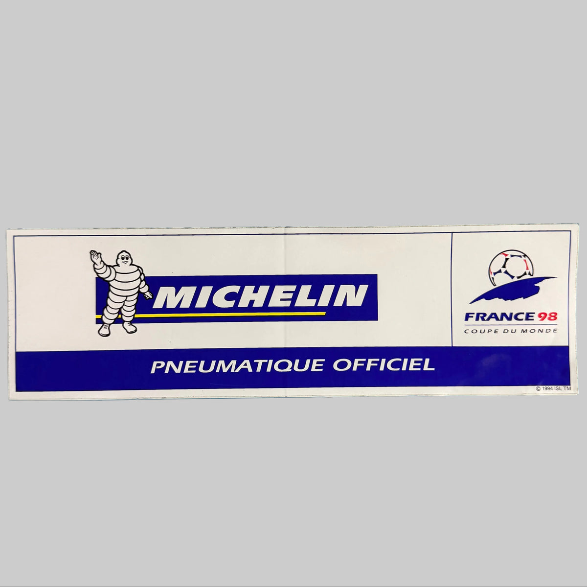 Autocollant publicitaire Michelin France 98 de 25 × 7,5 cm, représentant Bibendum, le logo Michelin, la mention Pneumatique officiel et l'emblème de la Coupe du monde 1998.