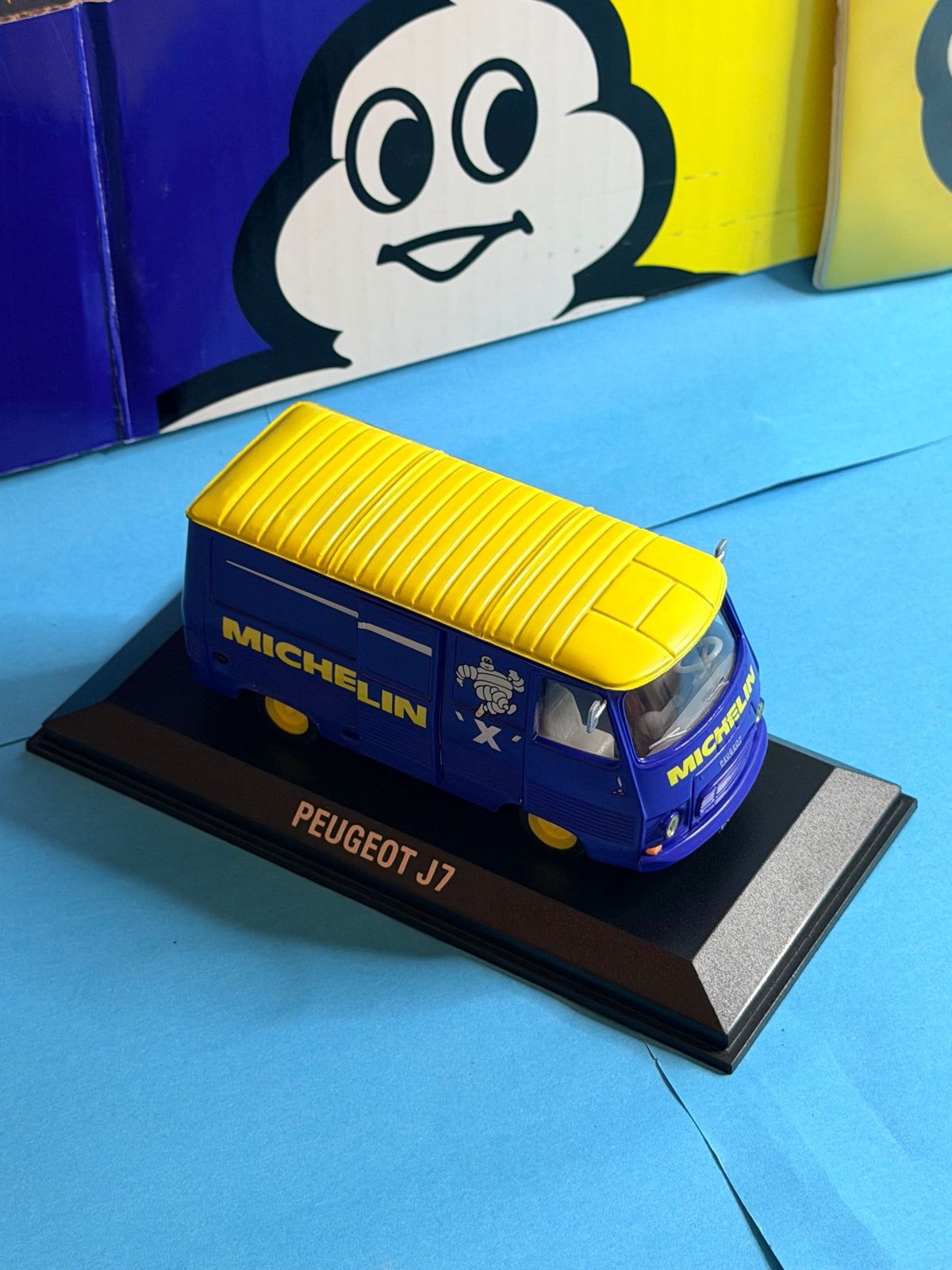 Vue trois quarts avant du Peugeot J7 Michelin miniature bleu et jaune avec logos Michelin et Bibendum.