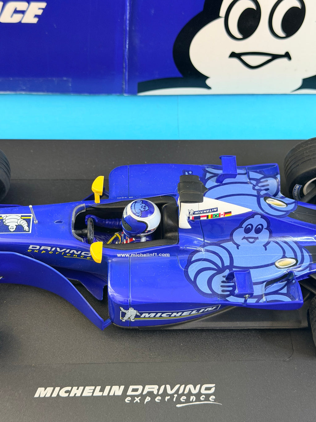 Gros plan sur le cockpit et la carrosserie de la Formule 1 Michelin avec pilote casqué et décoration rare Bibendum bleu.