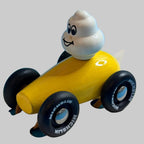 Voiture jaune Michelin Village avec Bibendum au volant, vue trois-quarts