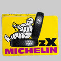 Autocollant Michelin ZX vintage avec Bibendum au volant, deux pneus et fond jaune, dimensions 15,7 × 11 cm.