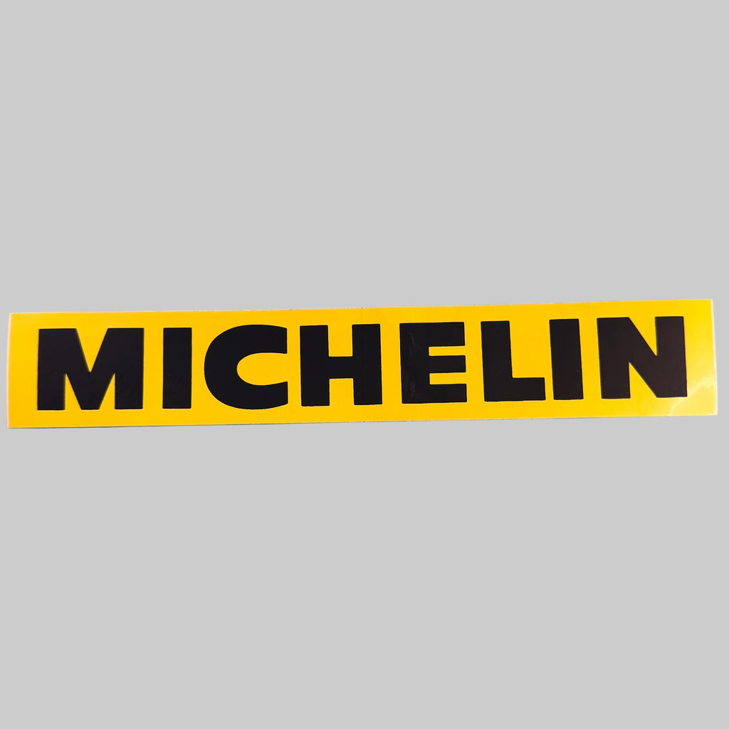 Autocollant publicitaire Michelin de 24 × 4 cm avec logo Michelin en grandes lettres noires sur fond jaune, photographié de face.