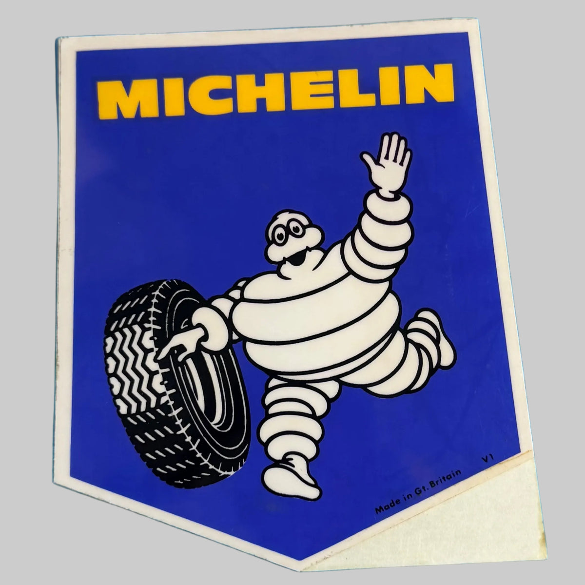 aAutocollant Michelin vintage bleu et jaune avec Bibendum saluant et tenant un pneu, fabrication britannique.