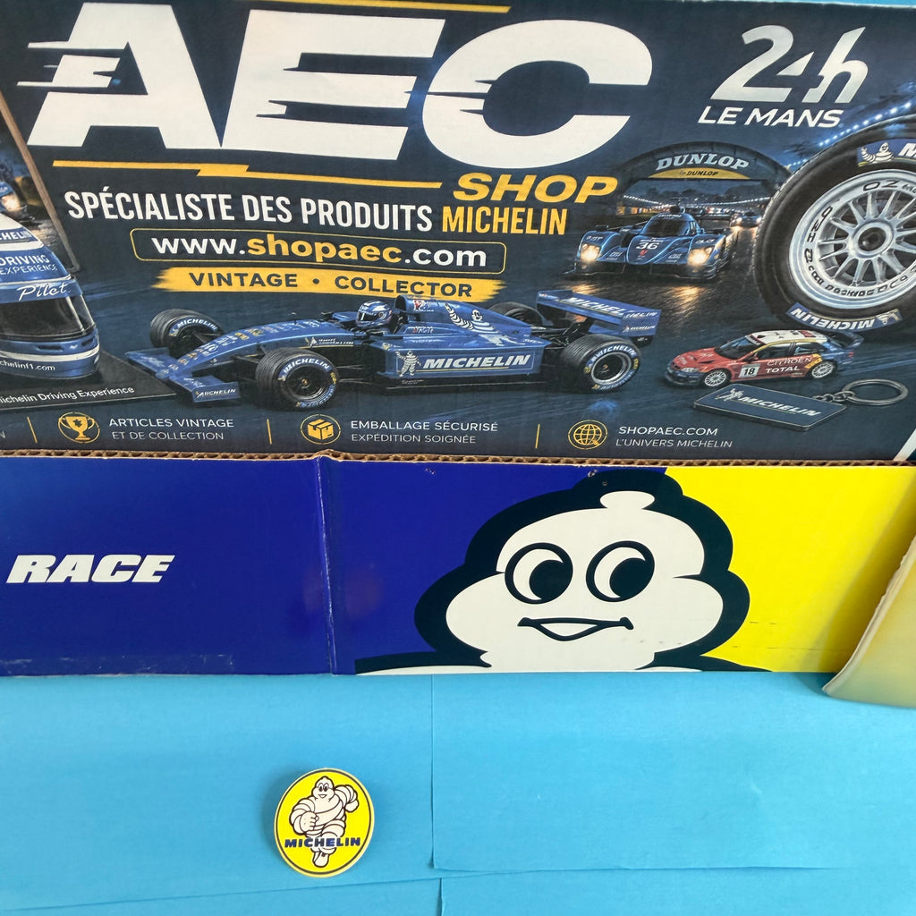 Badge publicitaire Michelin Bibendum aux couleurs emblématiques jaune et bleu, un accessoire de collection pour les passionnés de la marque française.