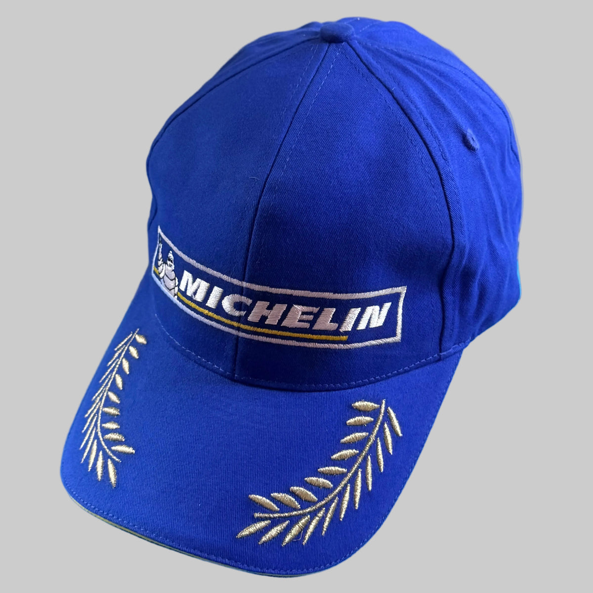 Casquette Michelin Podium neuve bleu et jaune avec Bibendum, logo Michelin et lauriers brodés sur la visière. Modèle collector pour passionnés.