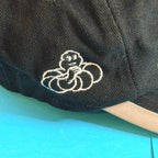 Gros plan sur le Bibendum Michelin brodé en fil clair sur le tissu noir de la casquette.