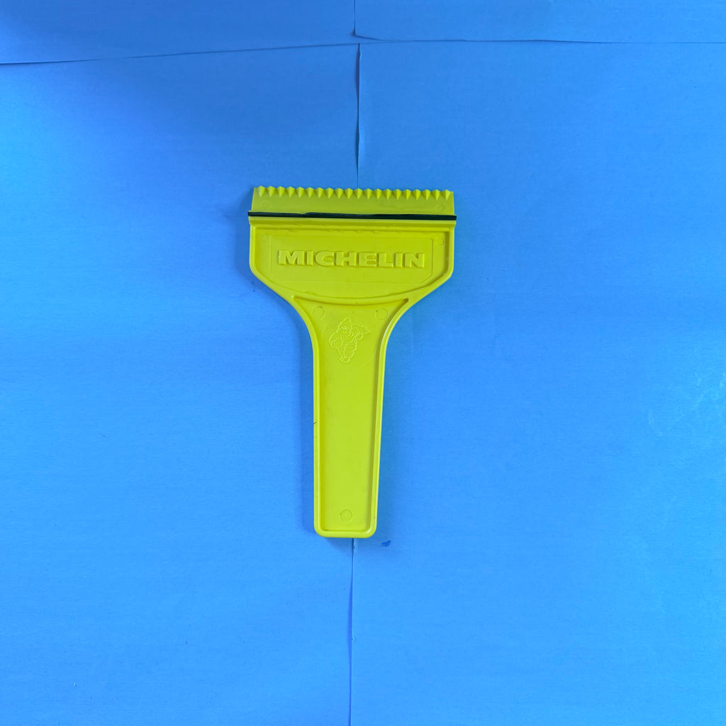 Gratte-pare-brise Michelin jaune neuf avec inscription MICHELIN en relief, Bibendum moulé sur le manche et bordure noire de raclage.