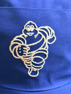 Gros plan sur le Bibendum Michelin brodé en blanc sur la face avant de la casquette bleue.