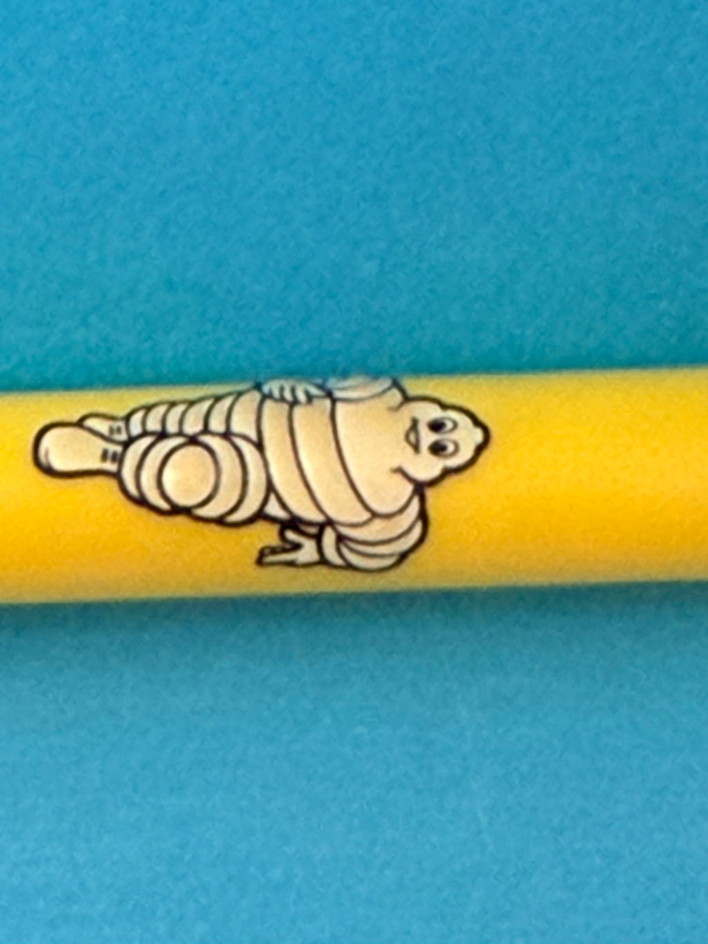 Détail du Bibendum Michelin blanc en relief sur stylo vintage jaune de collection
