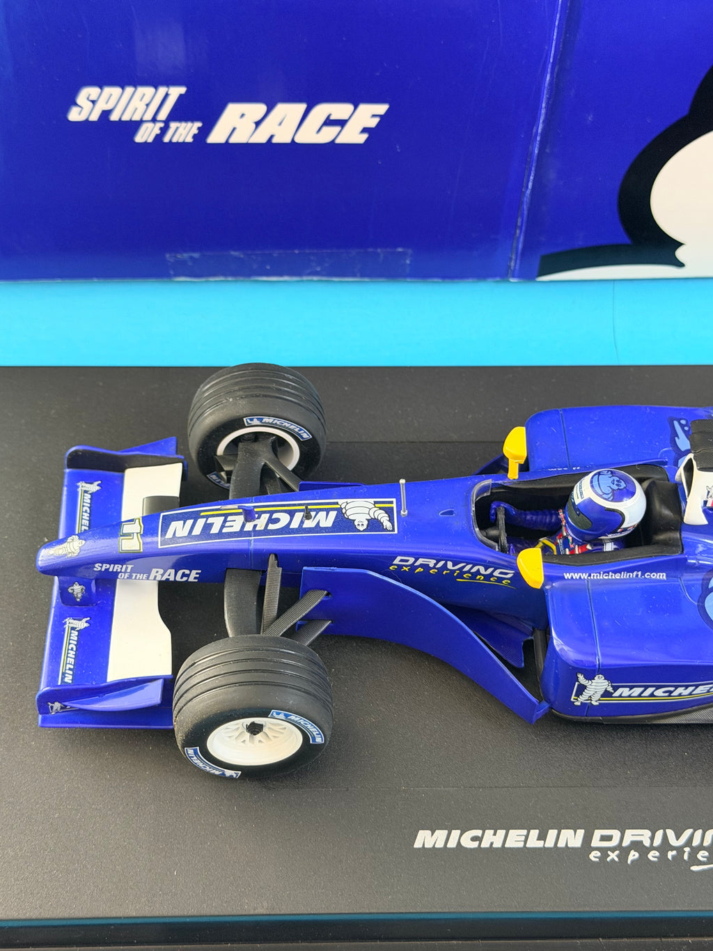 Gros plan sur le cockpit et la carrosserie de la Formule 1 Michelin avec pilote casqué et décoration rare Bibendum bleu.