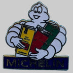 Pin's Michelin Bibendum tenant trois guides Michelin colorés, avec inscription Michelin sur fond bleu.