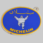 Autocollant Michelin ovale bleu et jaune avec Bibendum au centre, inscription arabe et logo Michelin.