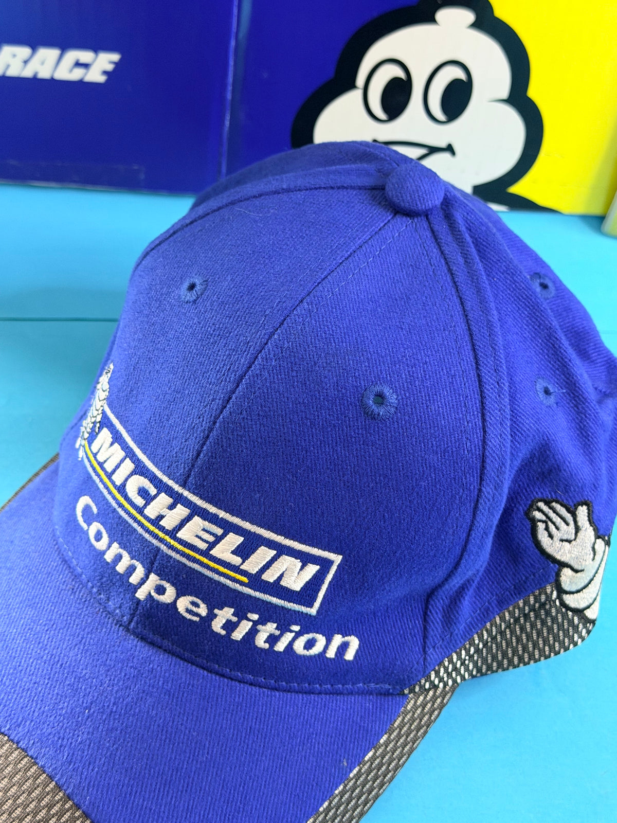 Détail de la broderie Michelin Competition et du Bibendum sur casquette bleue de collection.
