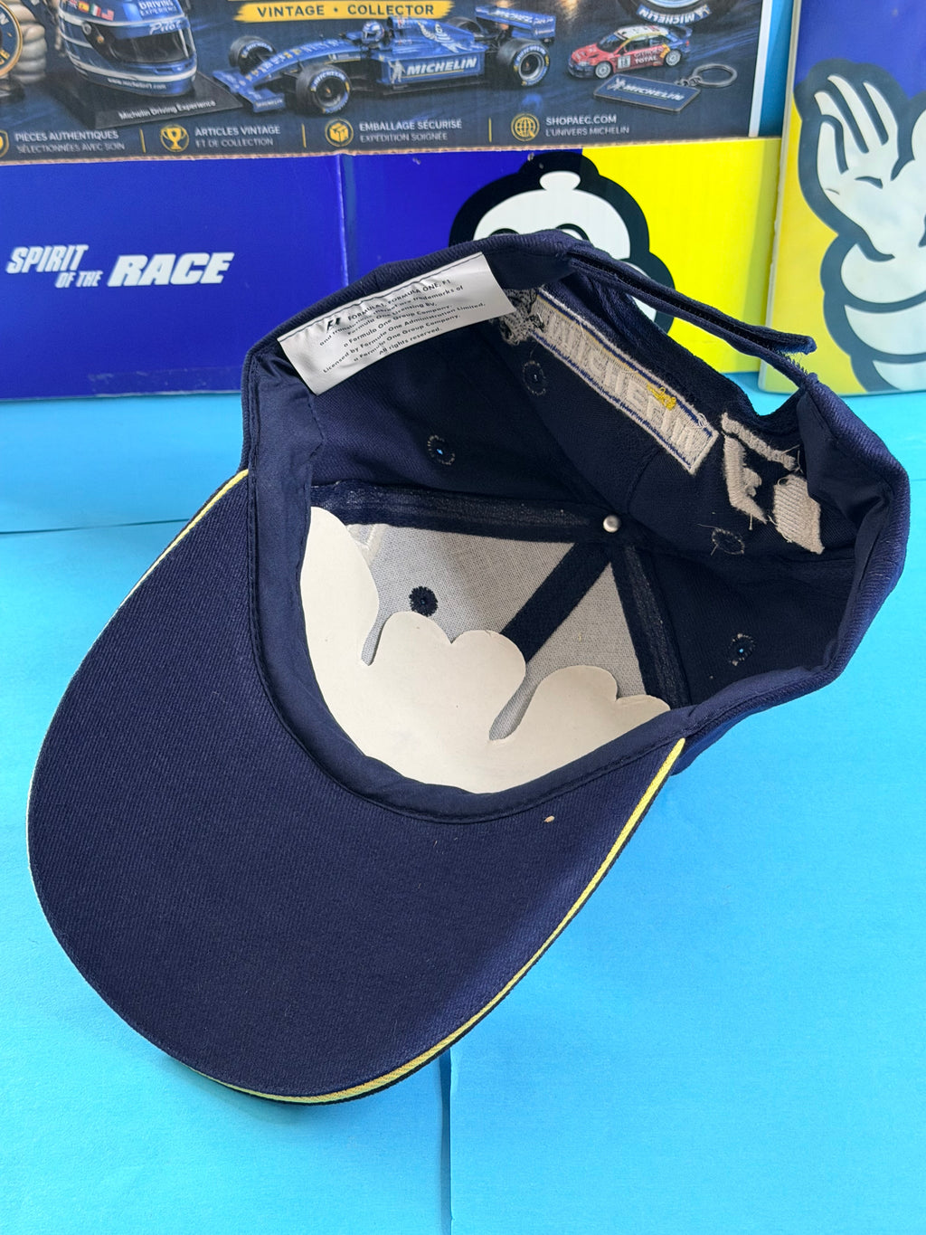 Vue intérieure de la casquette Michelin F1 Spirit of the Race neuve avec visière bleu marine bordée de jaune.